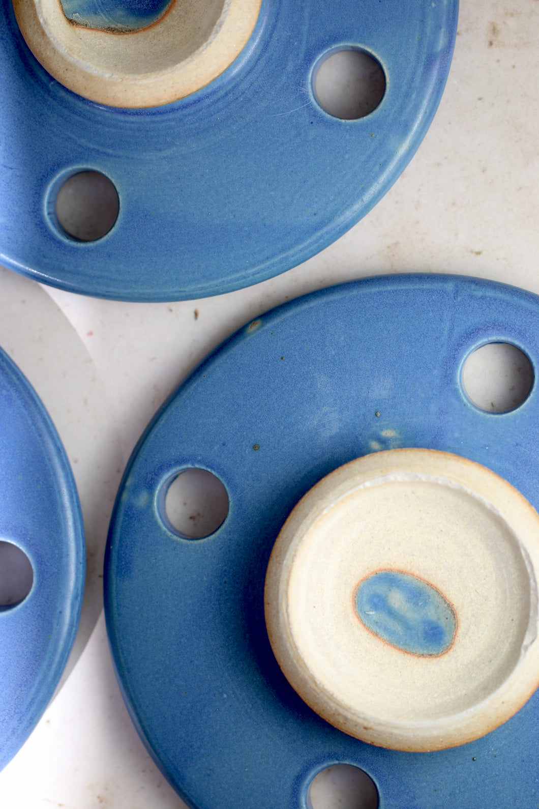 Bright royal blue ceramic cooking stone.  overhead image of a circular disc shaped cooking stone with an exposed ceramic handle laid on a beige counter